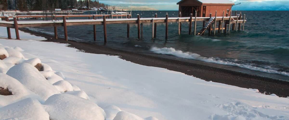 A snow-covered beach with a wooden pier leading to a cabin.