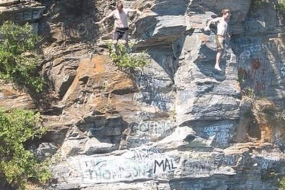 A rocky cliff with graffiti and a body of water at its base.