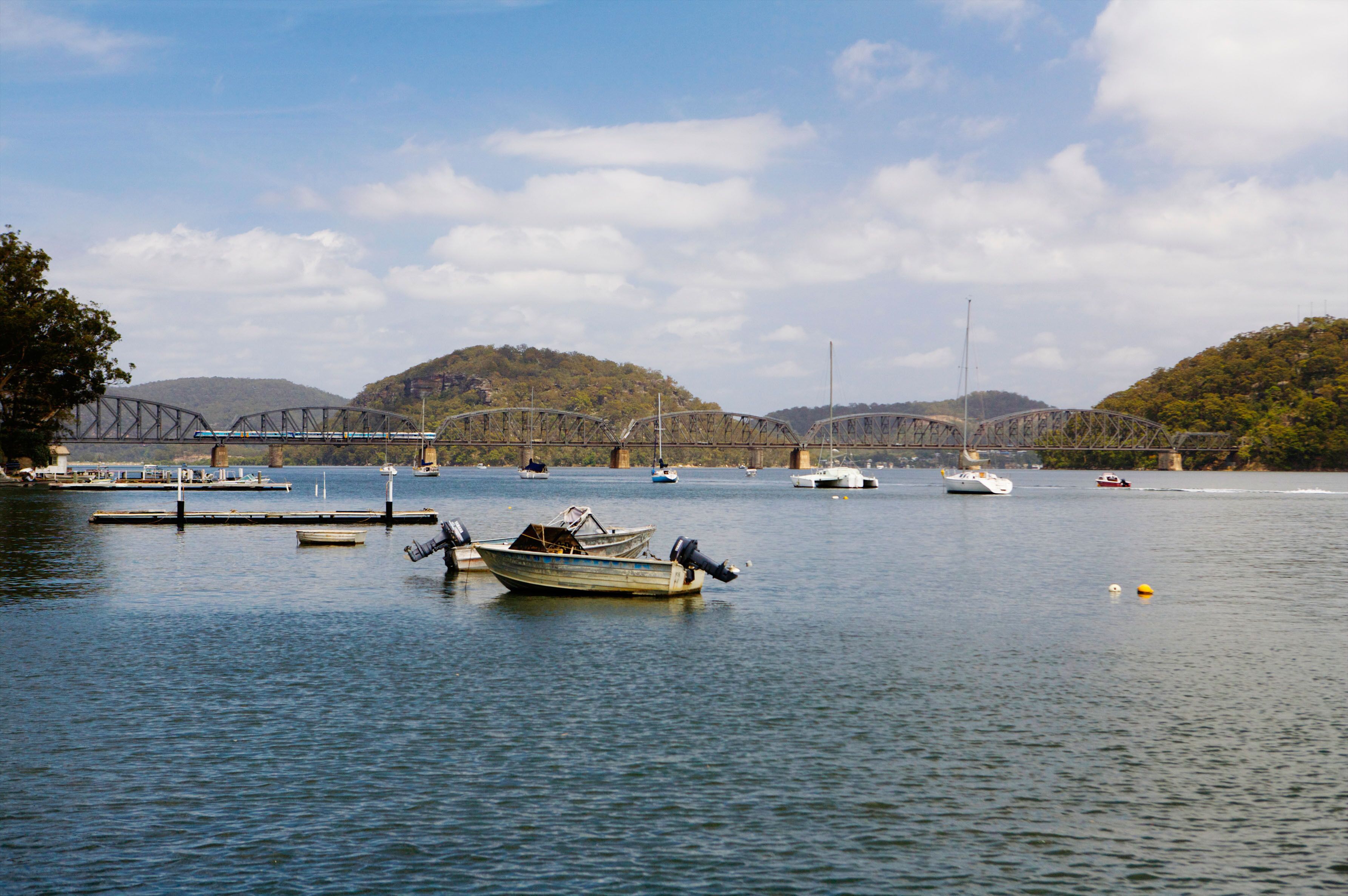 A calm lake with several boats, a bridge, and hills in the background.
