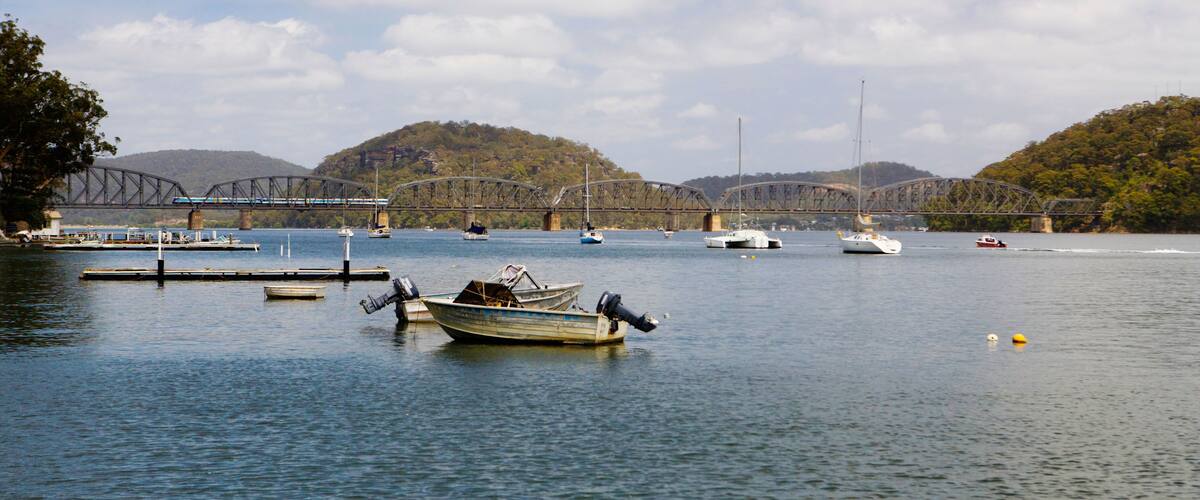 A calm lake with several boats, a bridge, and hills in the background.