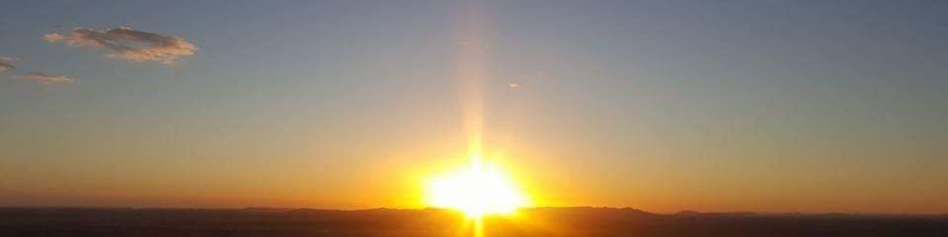 A sunset over a desert landscape with sand dunes.