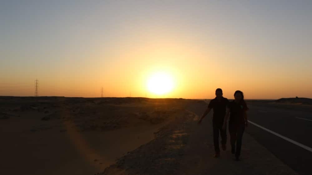 Two people walking on a road during sunset.