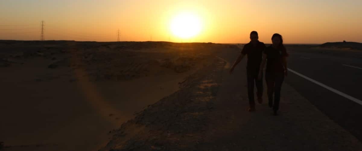 Two people walking on a road during sunset.