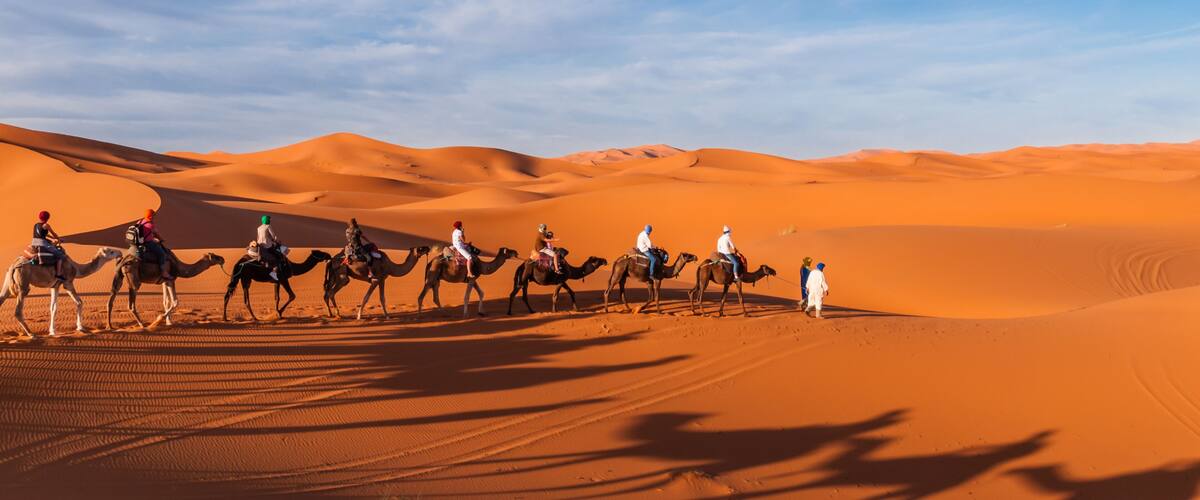 A group of people riding camels across a desert landscape with sand dunes under a clear sky.