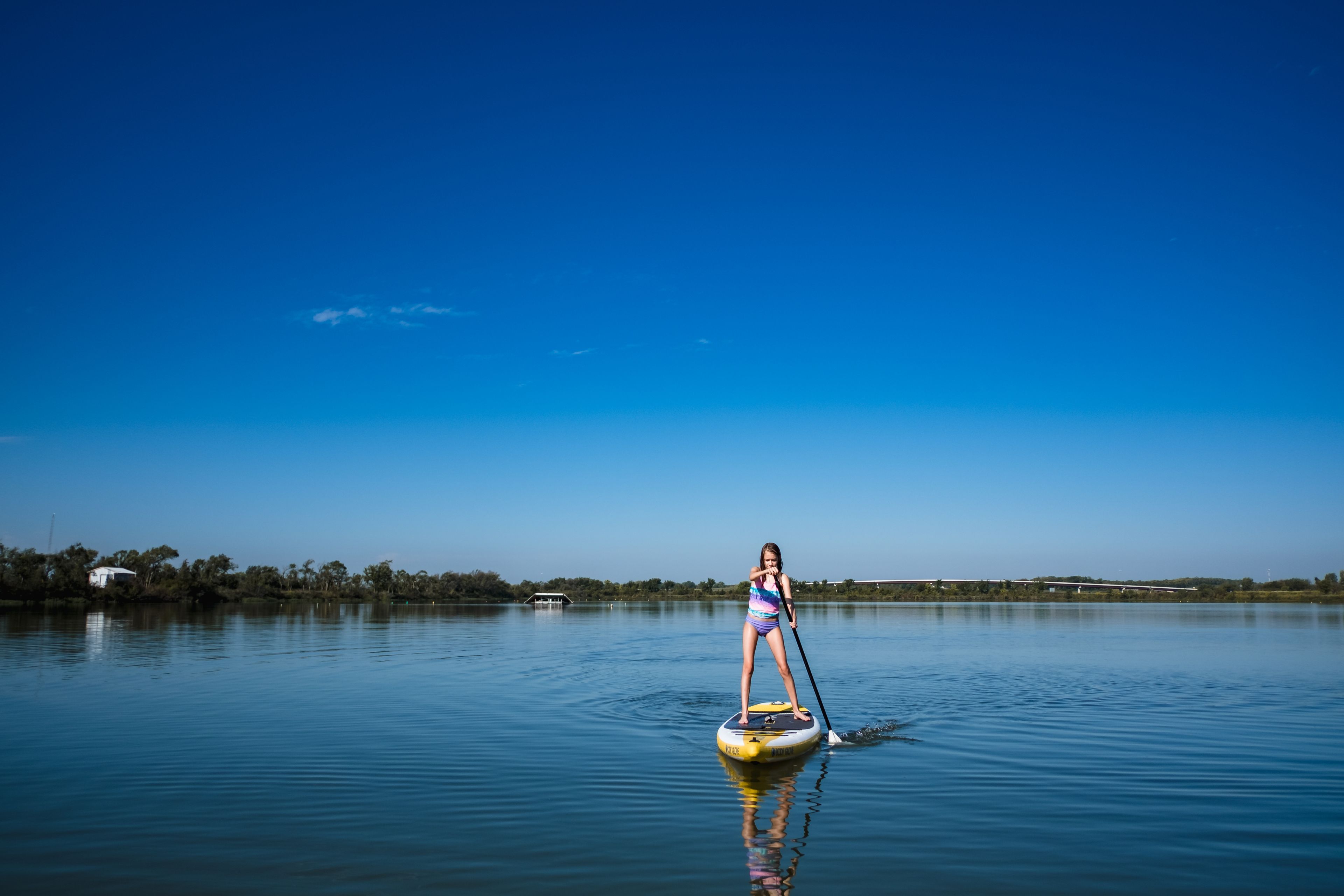 A person paddleboarding on a calm lake with a clear blue sky.