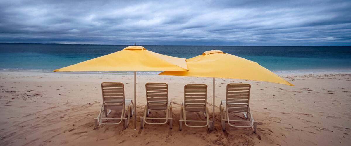 A beach with four lounge chairs and two yellow umbrellas.