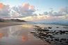 A beach with wet sand and scattered rocks, a cloudy sky, and distant hills.