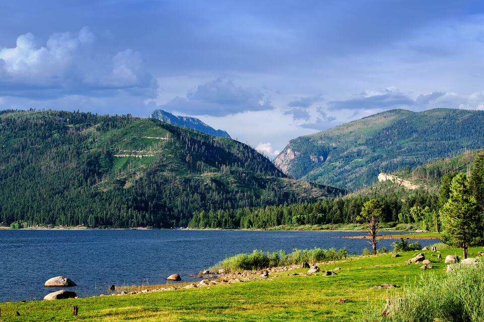 Un lac entouré de collines verdoyantes et bordé par une chaîne de montagnes boisée.