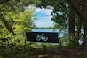 On a sunny Summer day, an empty bench with a bicycle design faces the Chippewa River from a shady spot along the Old Abe State Trail, near Jim Falls, WI.