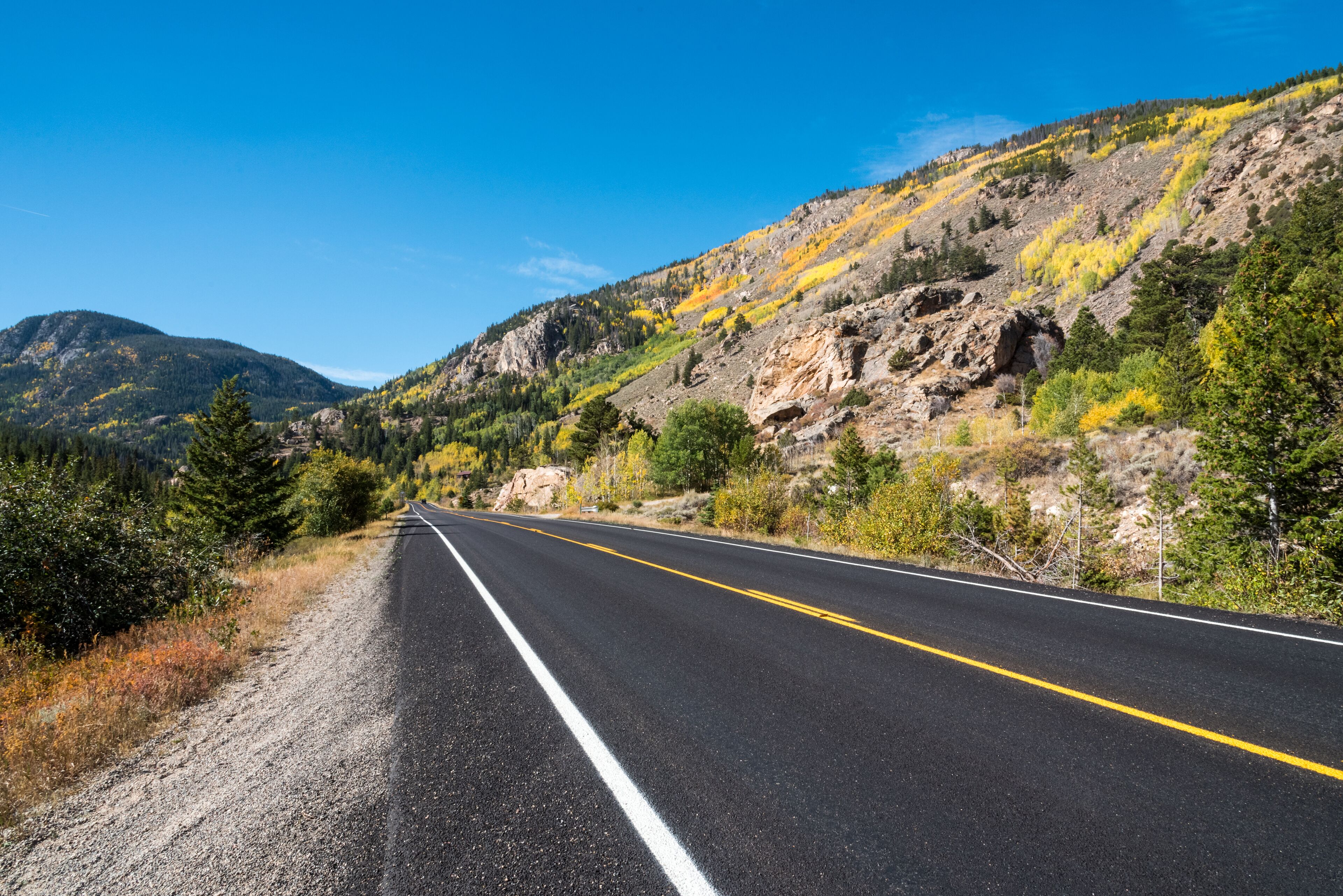A two-lane road with yellow dividing lines, surrounded by rocky hills and sparse vegetation.
