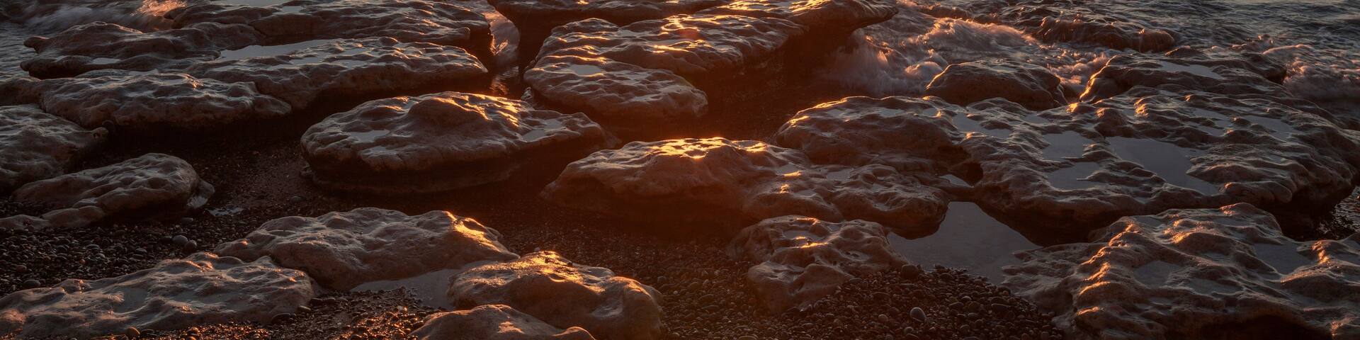 A sunset over a rocky shoreline with waves.