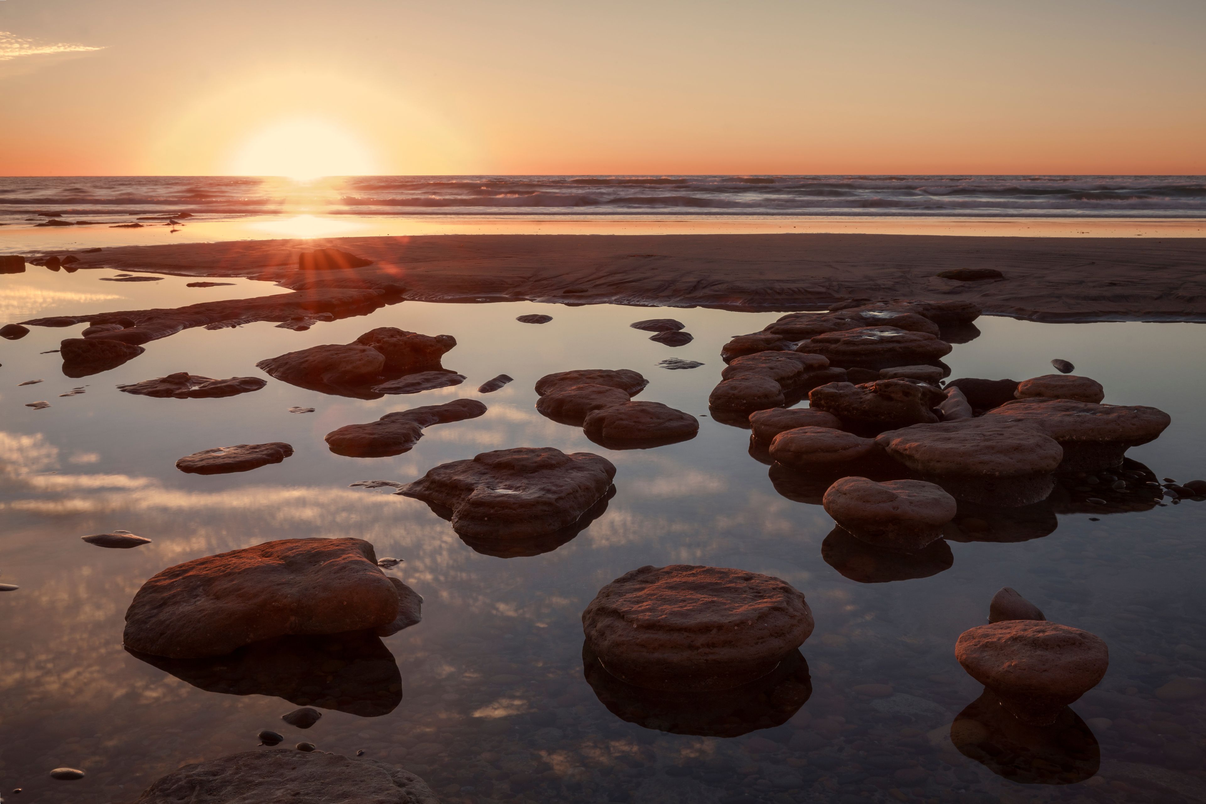 Une plage au coucher du soleil, avec des rochers dans l’eau.