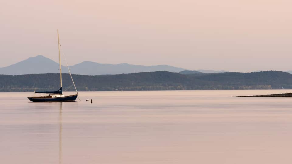 A calm lake with a sailboat and distant mountains.