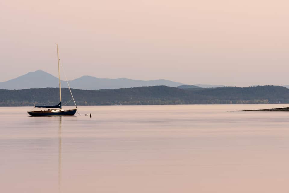 A calm lake with a sailboat and distant mountains.