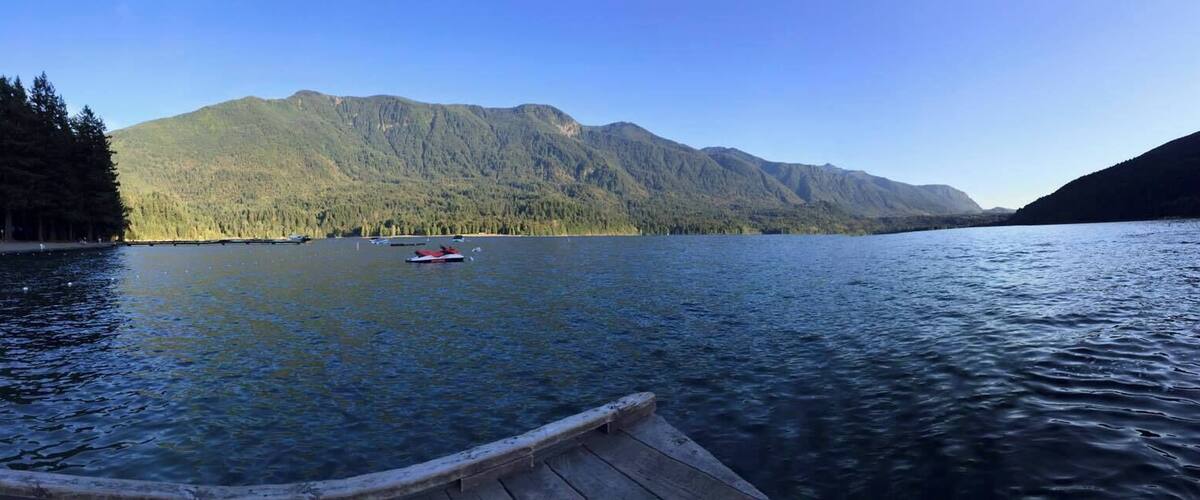 A calm lake with a boat, surrounded by forested mountains.