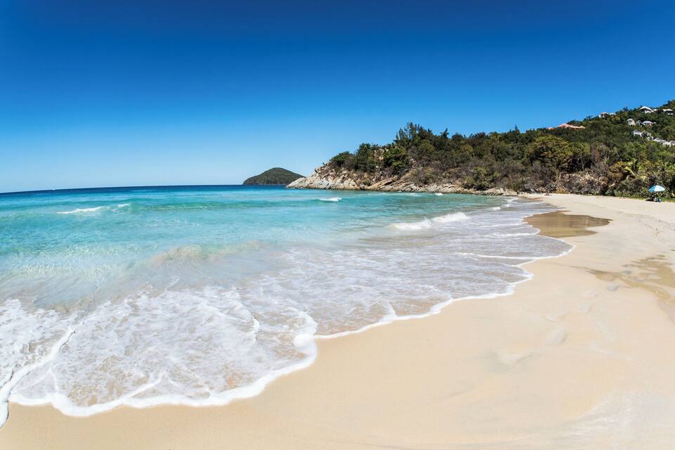 A beach with clear turquoise water, sandy shore, and a forested hillside.