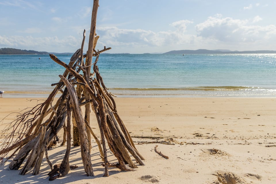 A beach with a pile of driftwood and a sign in the background.