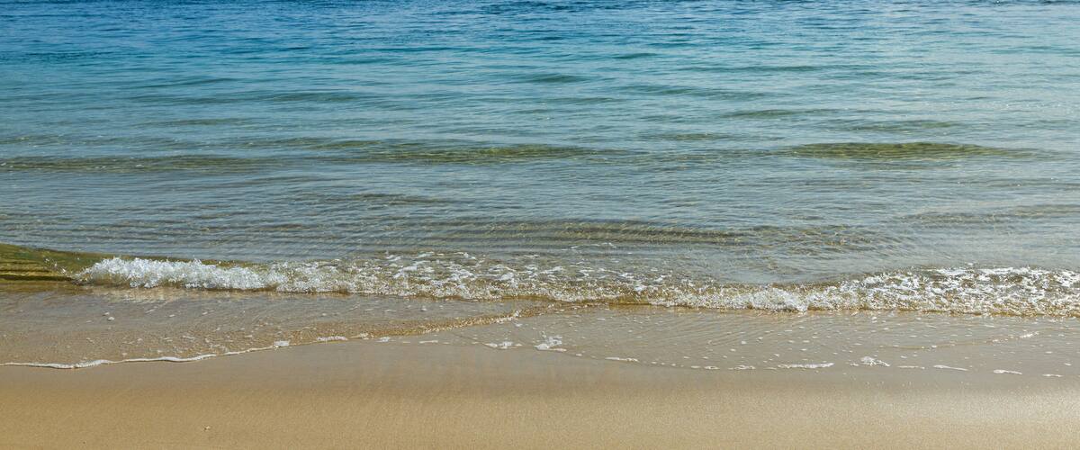 A beach with clear water, gentle waves, and distant landforms.