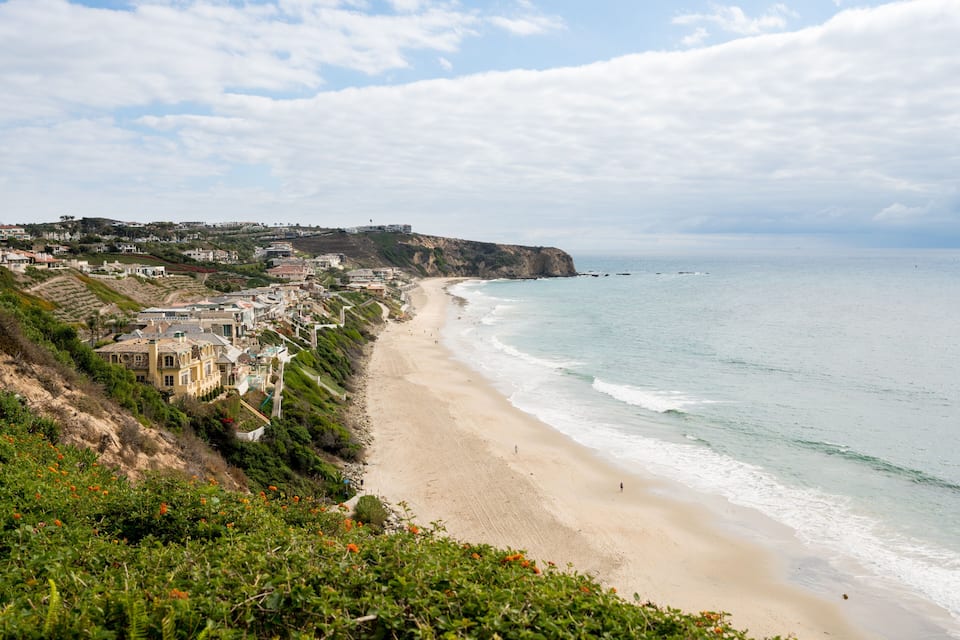 A coastal town with a sandy beach, houses along the cliff, and the ocean.