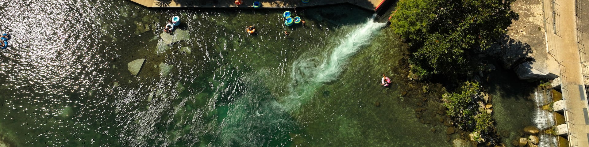 An aerial view of a river with clear water, surrounded by trees and a bridge.