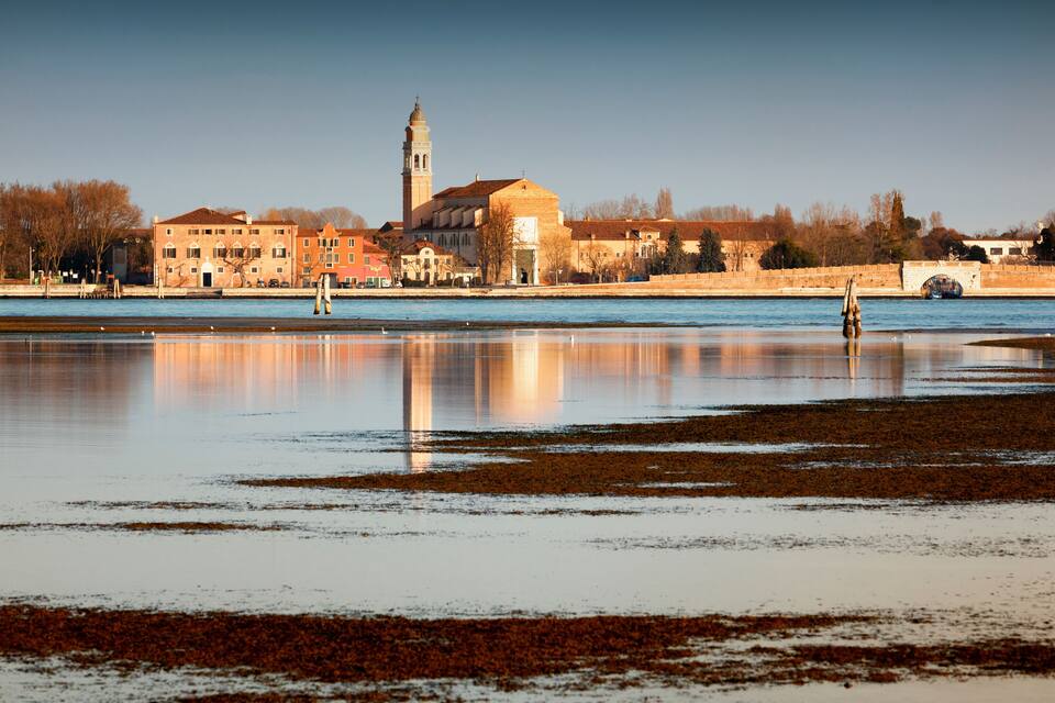 A frozen river with a reflection of buildings and a tower.