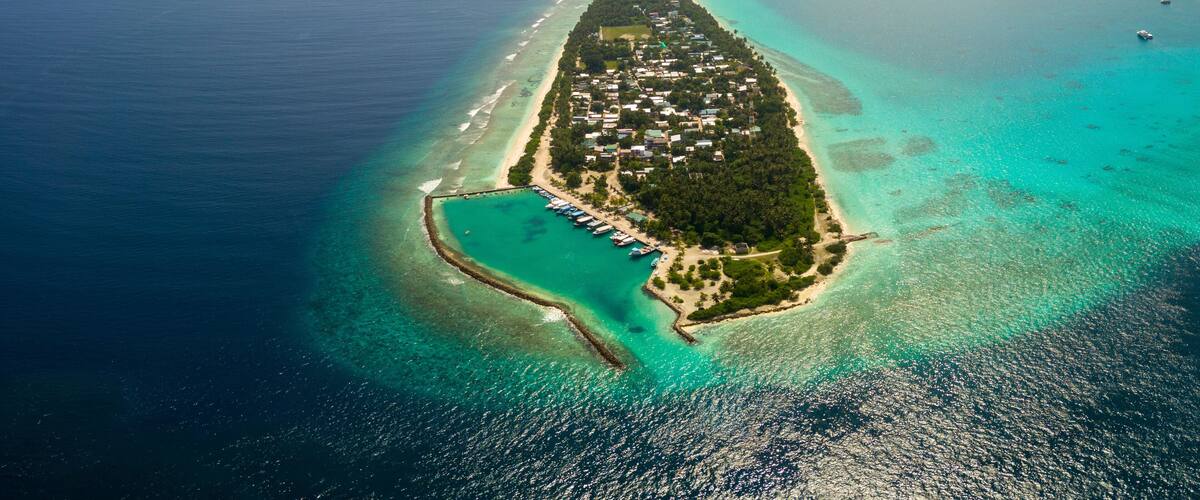An aerial view of a coastal island with clear turquoise waters, a dense forested area, and a long stretch of beach.