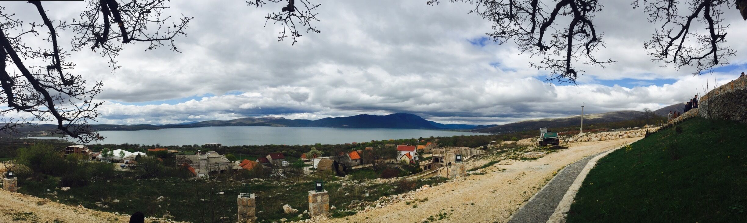 A coastal village with a lake, mountains in the background, and a dirt path leading through the landscape.