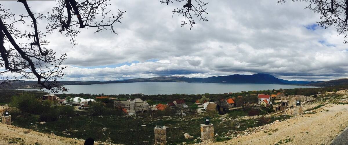 A coastal village with a lake, mountains in the background, and a dirt path leading through the landscape.