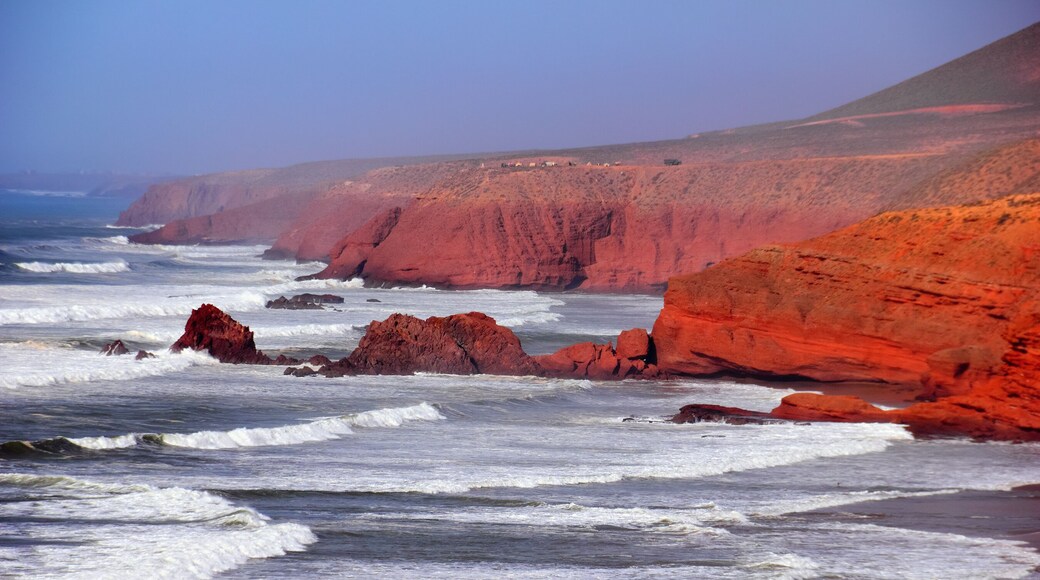 Rocky coast of Atlantic ocean, waves, sea surf, red rocks, ruins of famous mountain arch and blue evening sky. Beautiful nature view in Legzira beach, Sidi Ifni, Morocco, North West Africa.