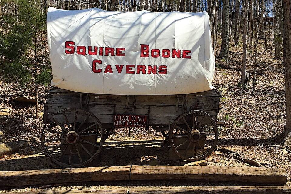 Ein beladener Wagen mit der Aufschrift 'SQUIRRE BOONE CAVERN', geparkt auf einem Kiesweg in einem bewaldeten Gebiet.