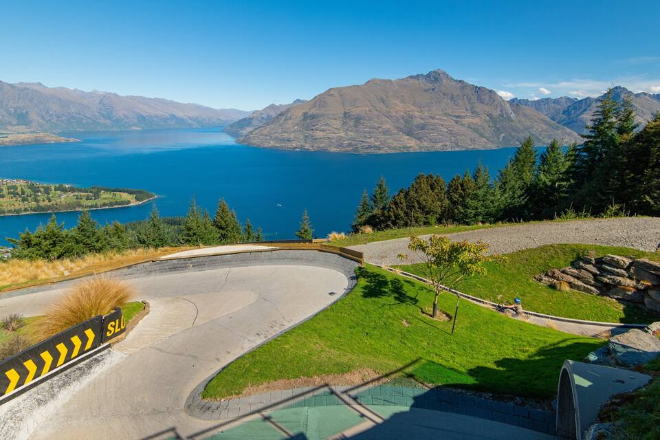 A winding road curving around a grassy area with a lake and mountains in the background.