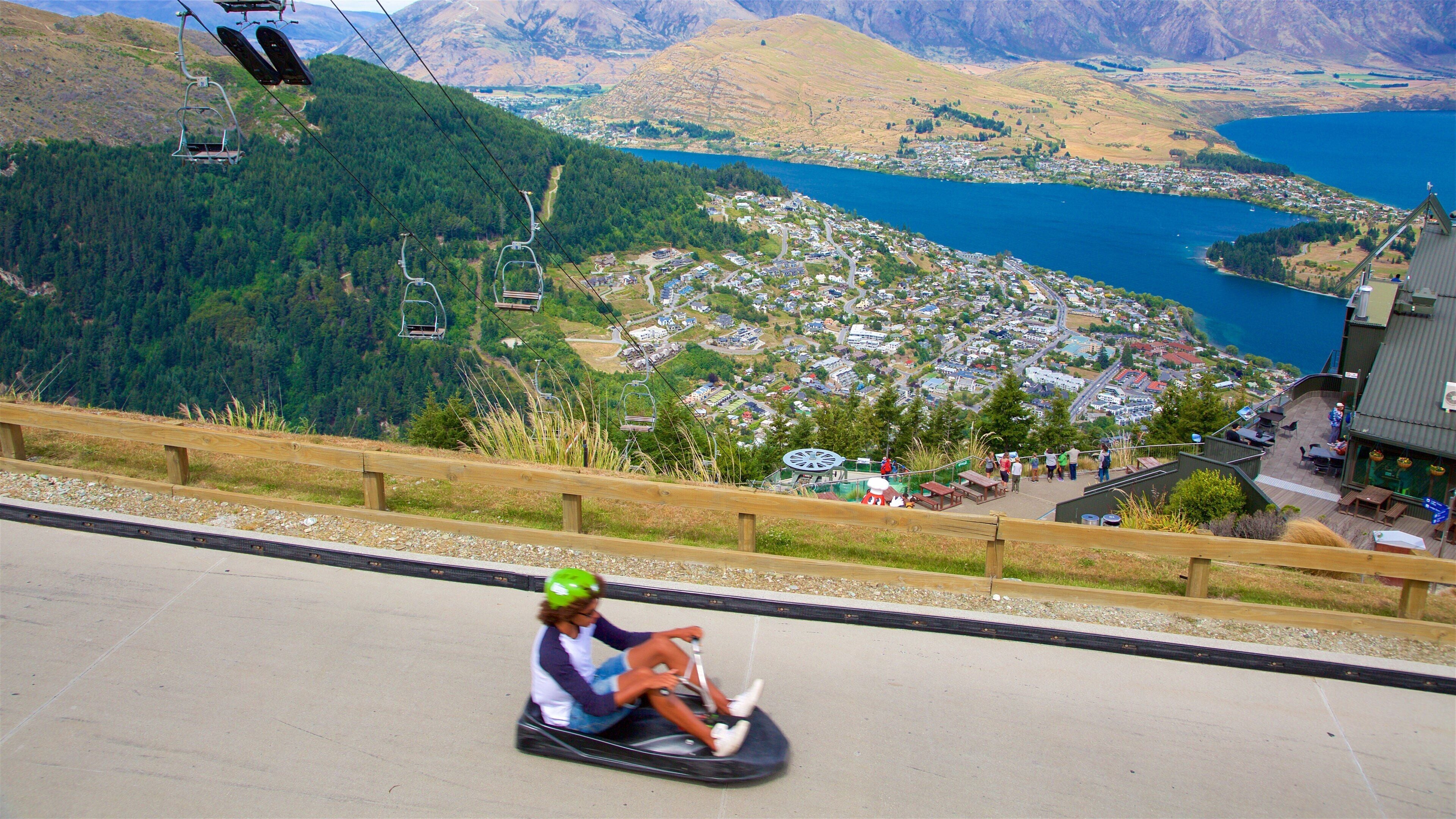 A person sledding down a snowy slope with a scenic view of a lake and a town in the background.
