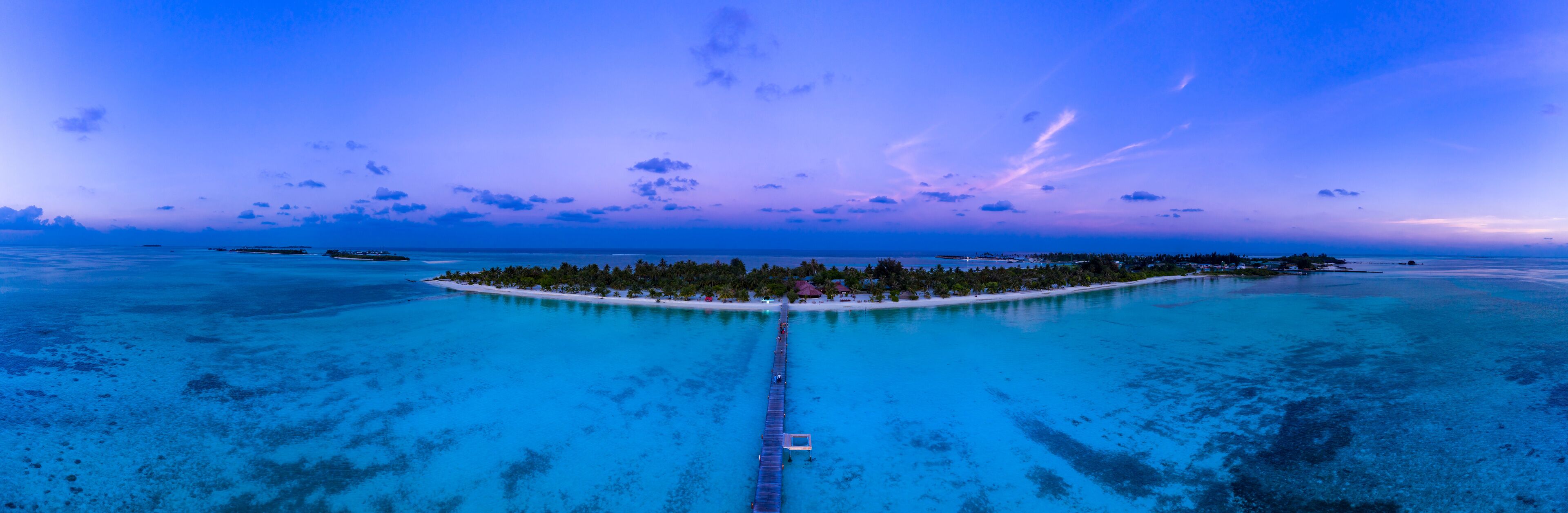 A tropical island with a white sandy beach, surrounded by turquoise waters, and a pier leading to the island.