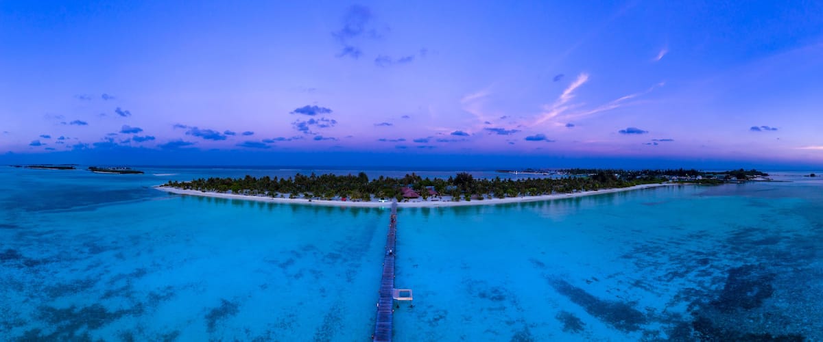 A tropical island with a white sandy beach, surrounded by turquoise waters, and a pier leading to the island.
