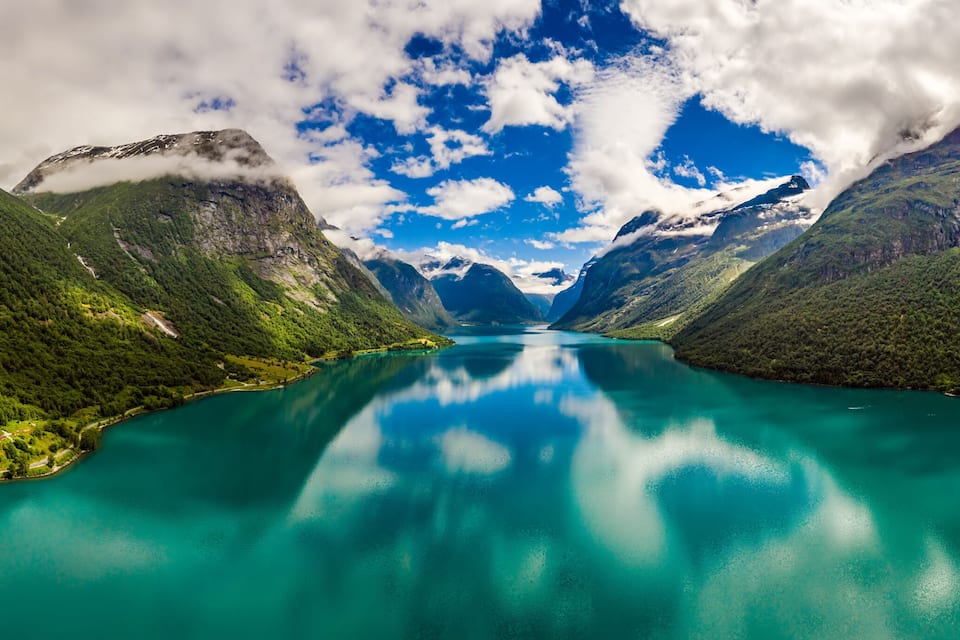 Ein türkisfarbener See, umgeben von üppigen, grünen Bergen und wolkenlosem Himmel.