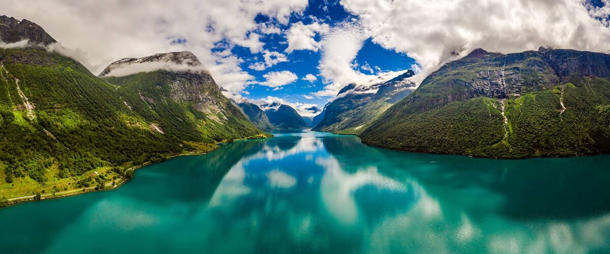 A turquoise lake surrounded by lush green mountains and a clear sky.