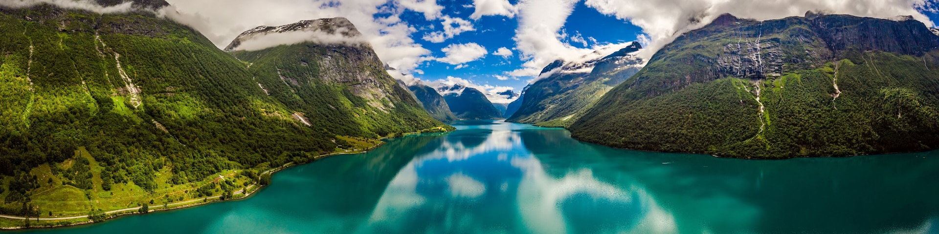 A turquoise lake surrounded by lush green mountains and a clear sky.
