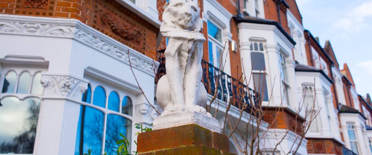 Statue of a lion in white stone in front of a row of restored luxury Victorian houses in red bricks and white finishing on a local street in London, UK
