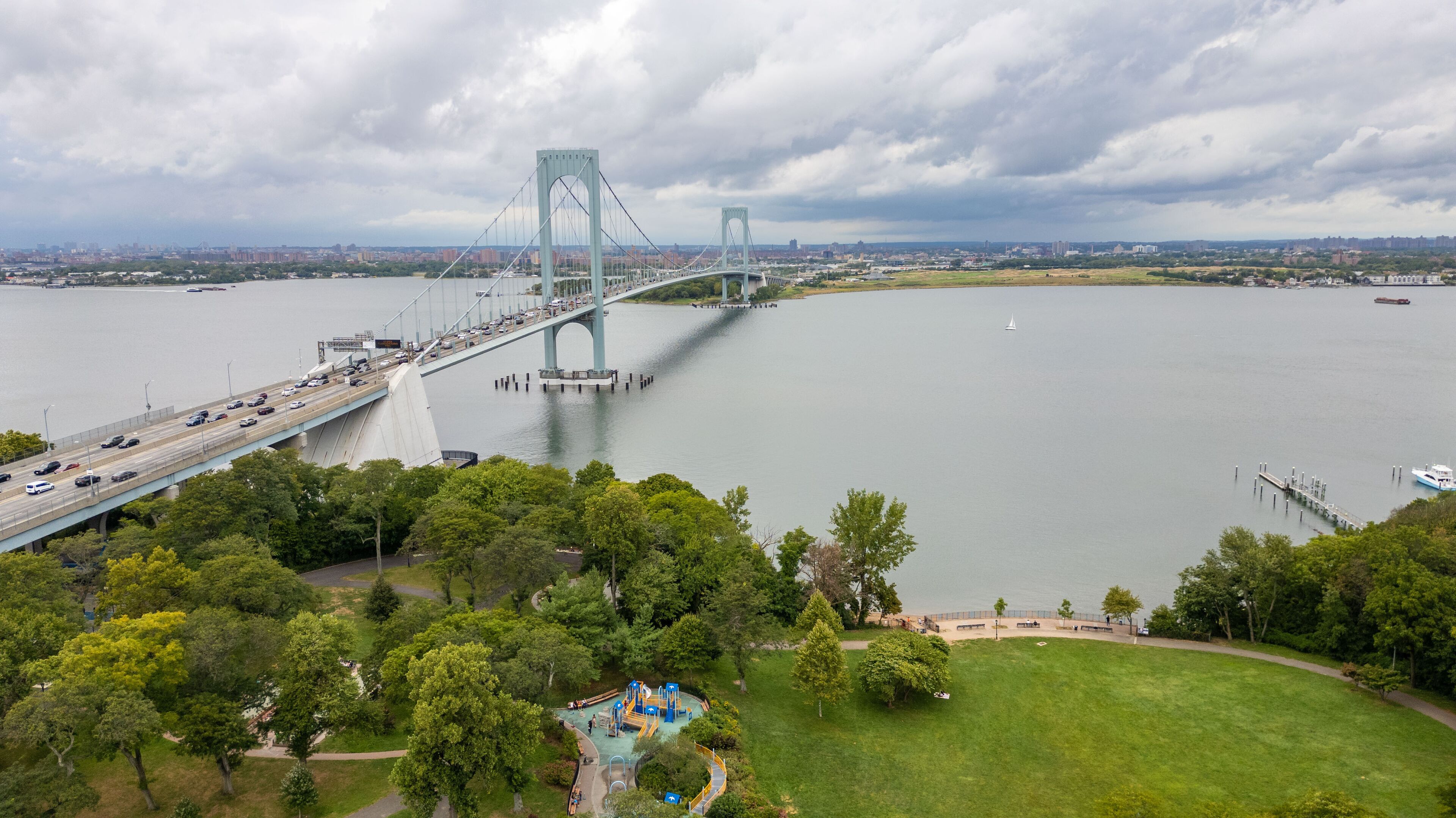 A large suspension bridge over a river with a park and playground in the foreground.