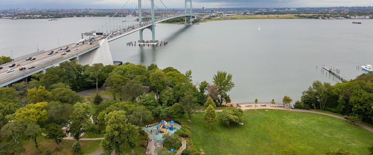 A large suspension bridge over a river with a park and playground in the foreground.