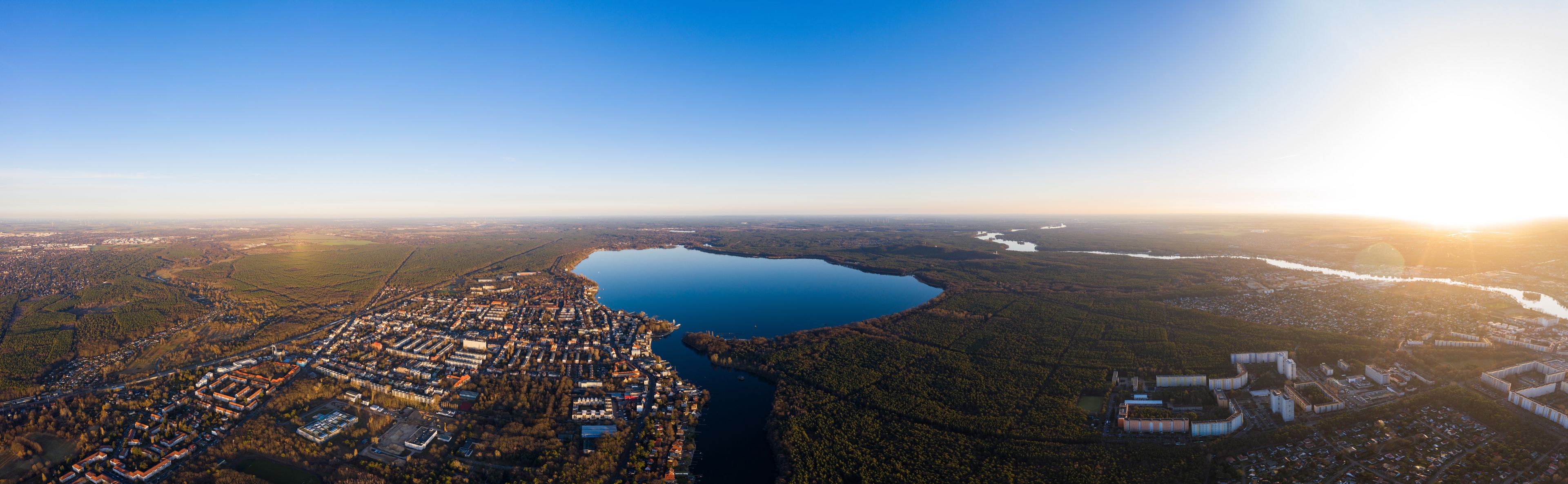 Luftaufnahme einer Stadt mit einem großen See, umgeben von bewaldeten Gebieten und Industriegebäuden.