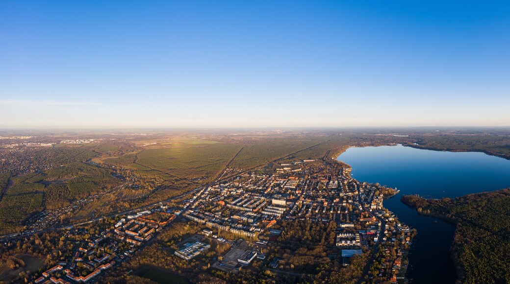 Luftaufnahme einer Stadt mit einem großen See, umgeben von bewaldeten Gebieten und Industriegebäuden.
