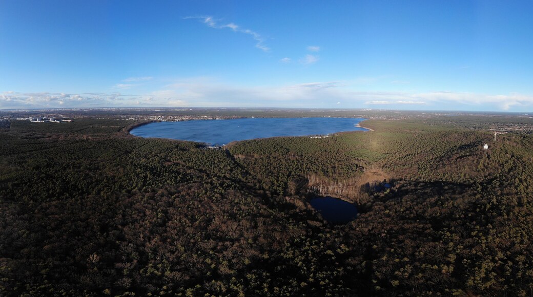 Weite, bewaldete Landschaft mit einem großen See und einer kleinen Stadt in der Ferne.
