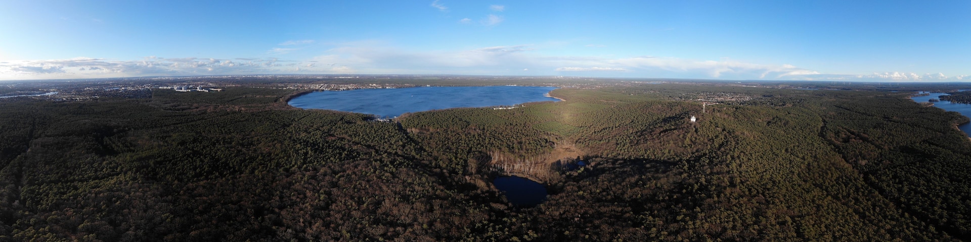 Weite, bewaldete Landschaft mit einem großen See und einer kleinen Stadt in der Ferne.