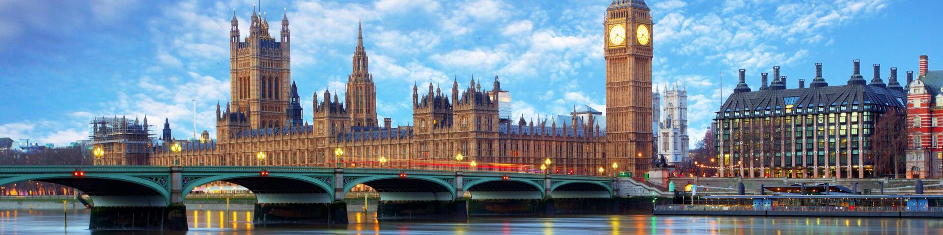 The Houses of Parliament and Big Ben in London, with the River Thames and a green bridge in the foreground.