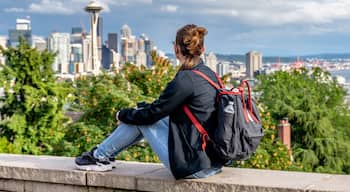SEATTLE, WASHINGTON, USA. Young lady backpacker tourist alike visiting Queen Anne Hill's Kerry Park to catch a spring sunset over downtown Seattle and Mt. Rainier in the background.