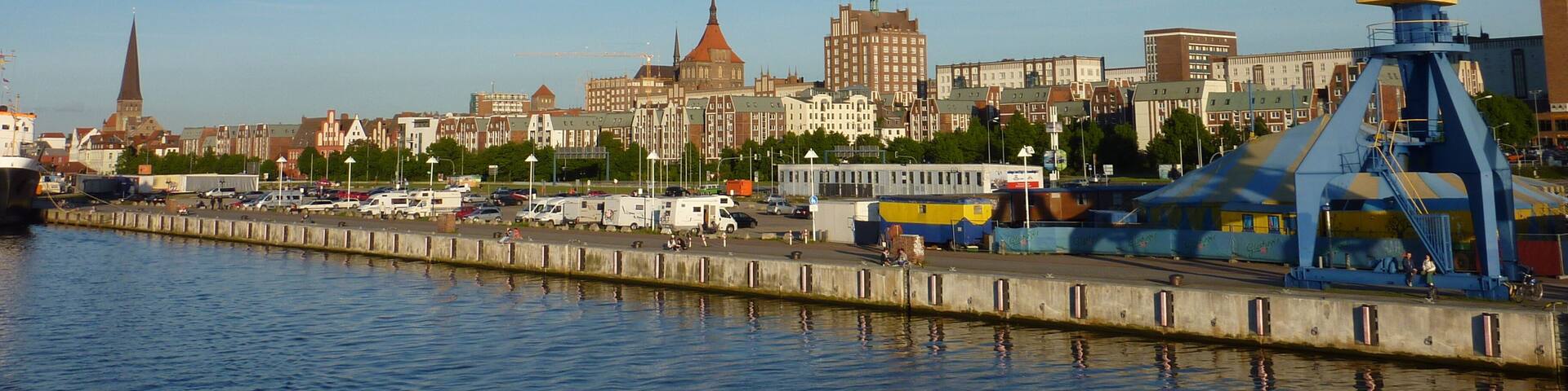 A waterfront cityscape with historic buildings, a crane, and hot air balloons.
