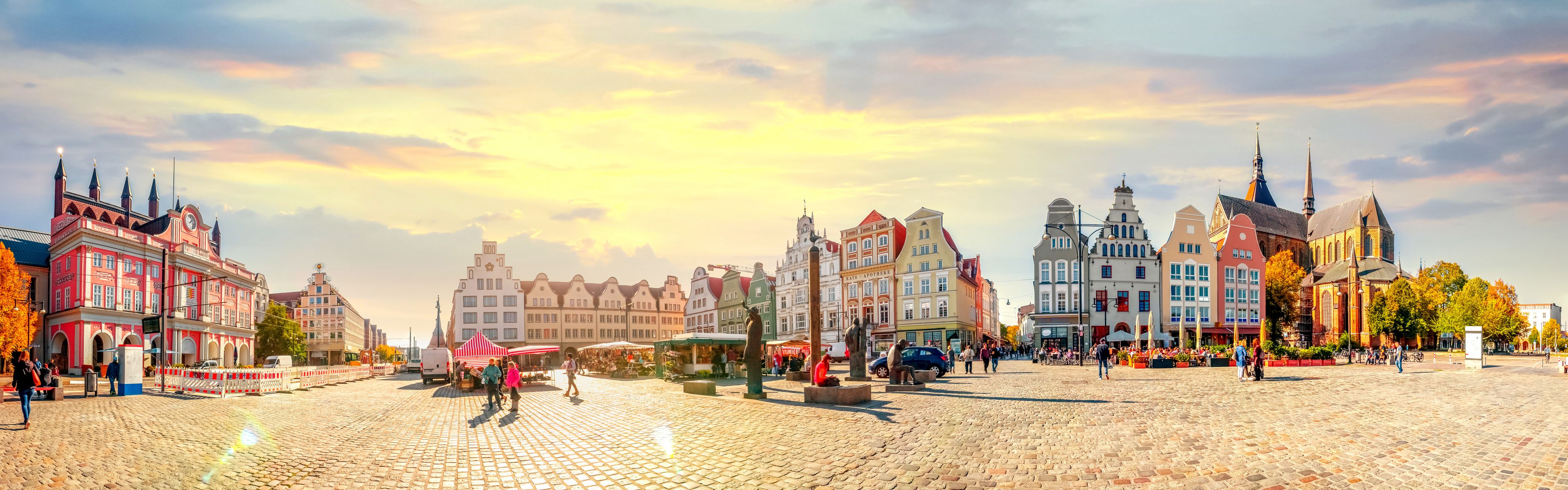 A cobblestone square with historic buildings, a church, and a market.
