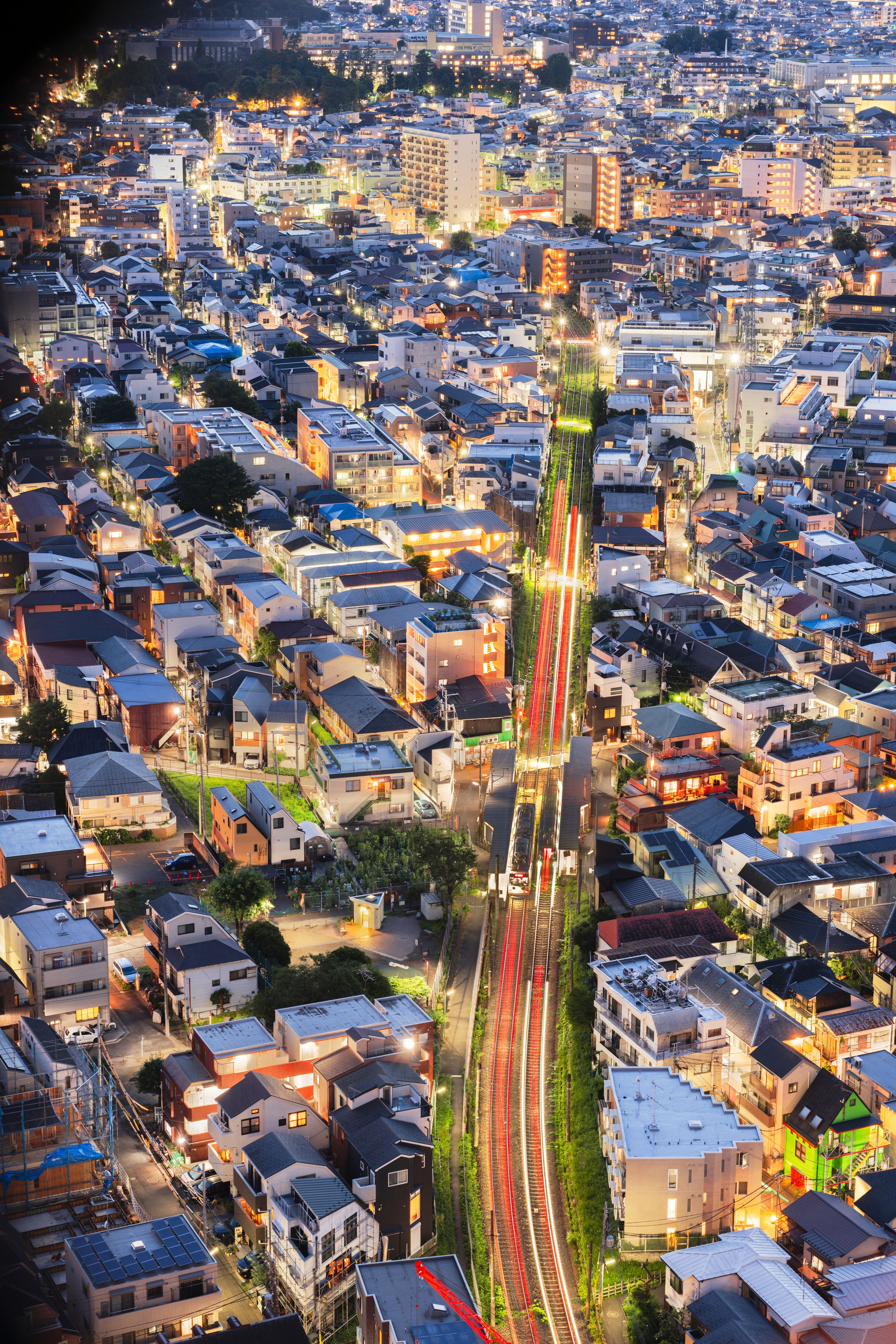 A cityscape at dusk with a prominent train track running through the center, surrounded by densely packed residential buildings.