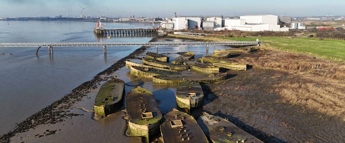 A coastal area with boats, a pier, and industrial buildings in the background.